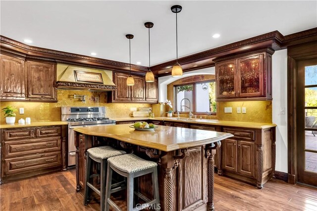 kitchen with stainless steel range with gas cooktop, custom exhaust hood, light countertops, dark wood-type flooring, and ornamental molding