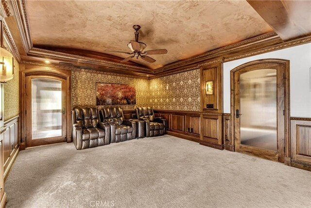 carpeted living room featuring a ceiling fan, crown molding, a wainscoted wall, a decorative wall, and a raised ceiling
