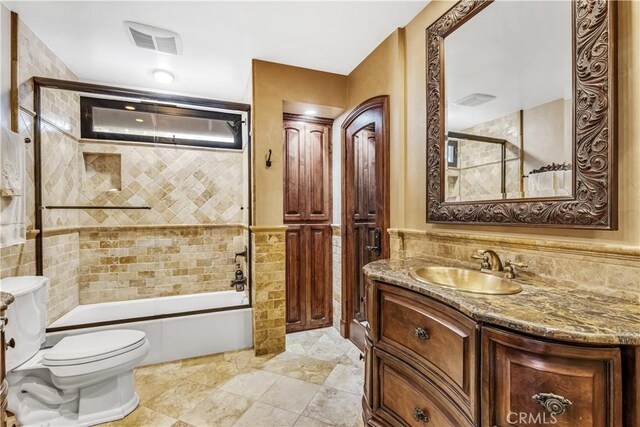bathroom with toilet, tile walls, vanity, shower / bath combination with glass door, and wainscoting