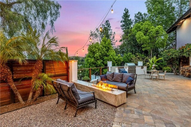 patio terrace at dusk with exterior kitchen and an outdoor living space with a fire pit
