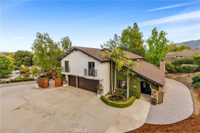 view of property exterior with a balcony, concrete driveway, stucco siding, an attached garage, and a shingled roof