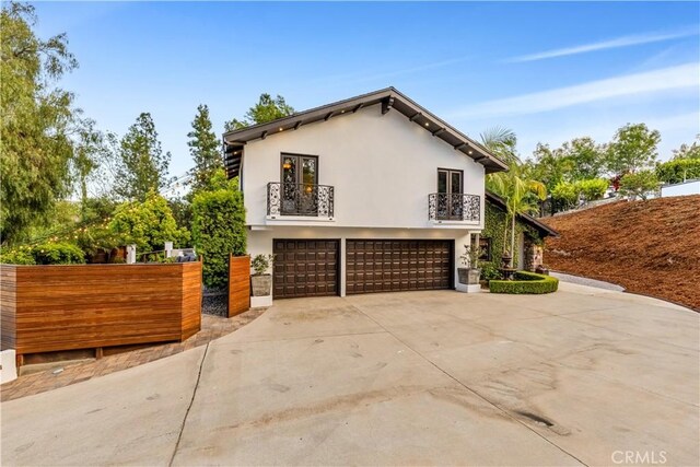 view of side of home featuring a balcony, a garage, stucco siding, driveway, and fence