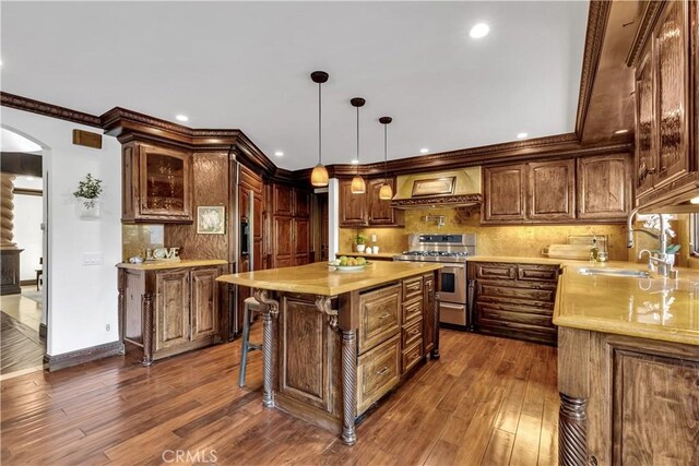 kitchen with range with two ovens, custom exhaust hood, arched walkways, a sink, and decorative backsplash