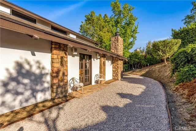 view of side of home featuring stone siding, stucco siding, a chimney, french doors, and a patio area
