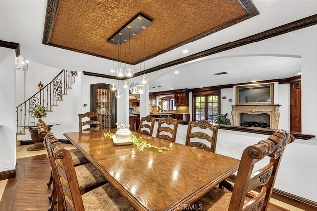 dining space with arched walkways, a tray ceiling, ornamental molding, baseboards, and a lit fireplace