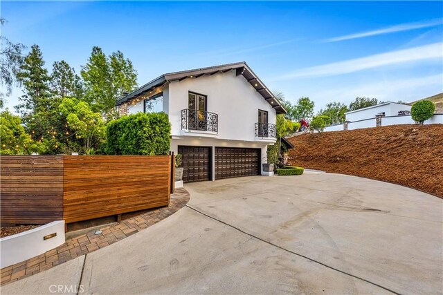 view of side of home featuring a balcony, an attached garage, concrete driveway, fence, and stucco siding