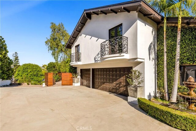 view of side of home featuring a balcony, stucco siding, an attached garage, and driveway