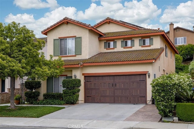mediterranean / spanish house with an attached garage, driveway, a tile roof, and stucco siding