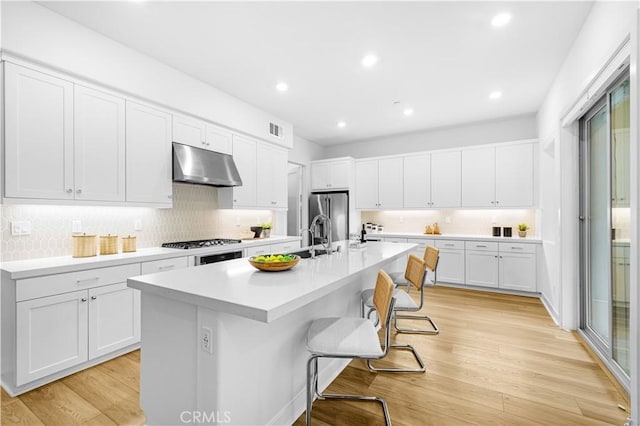 kitchen featuring under cabinet range hood, stainless steel fridge with ice dispenser, a kitchen bar, backsplash, and light countertops