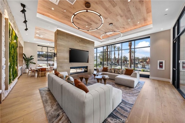 living area featuring a raised ceiling, wooden ceiling, recessed lighting, light wood finished floors, and baseboards