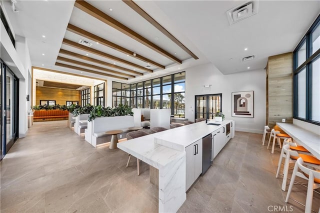 kitchen featuring modern cabinets, a large island with sink, a high ceiling, recessed lighting, and light stone counters