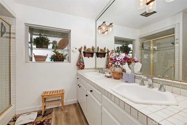 full bath with a stall shower, wood finished floors, double vanity, and baseboards