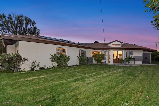 14321 Mimosa Ln, Tustin, CA 92780 - back of property at dusk with stucco siding, a yard, solar panels, and cooling unit