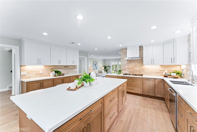 kitchen with wall chimney range hood, stainless steel appliances, a sink, recessed lighting, and a kitchen island
