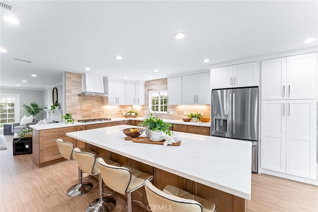 kitchen featuring appliances with stainless steel finishes, wall chimney range hood, tasteful backsplash, light countertops, and a breakfast bar area