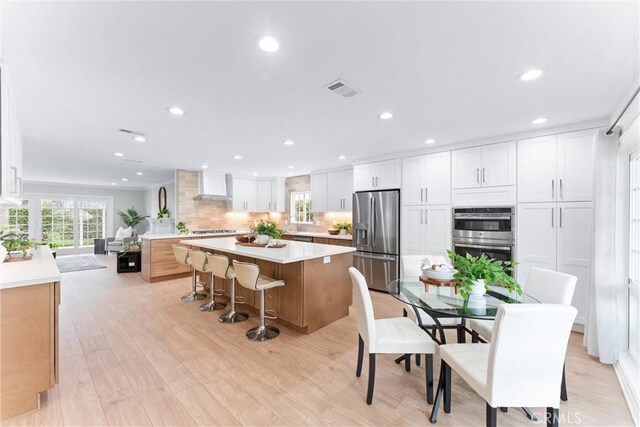 kitchen featuring stainless steel appliances, wall chimney range hood, a center island, recessed lighting, and white cabinetry