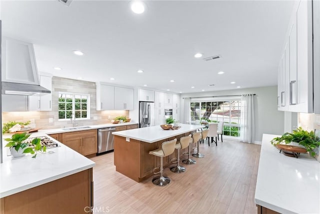 kitchen featuring stainless steel appliances, a sink, a breakfast bar, a kitchen island, and light wood-style floors