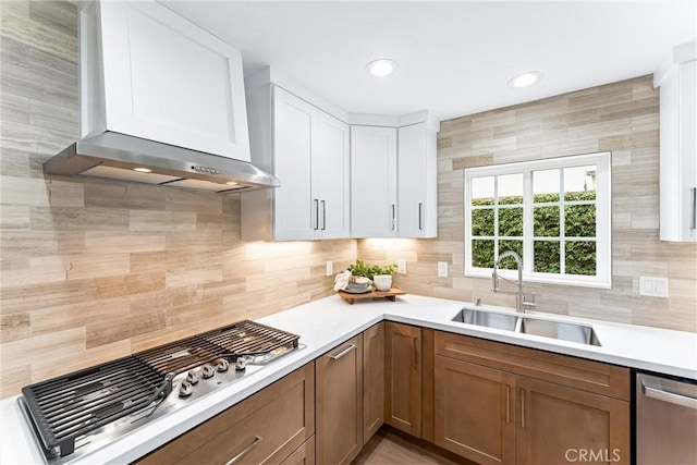 kitchen featuring wall chimney range hood, a sink, appliances with stainless steel finishes, decorative backsplash, and recessed lighting
