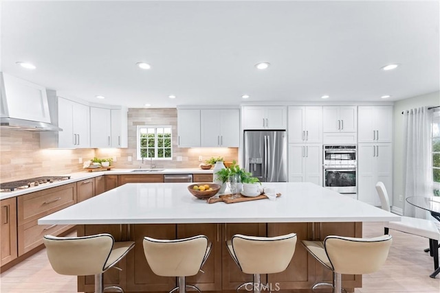 kitchen with stainless steel appliances, wall chimney range hood, a center island, a kitchen bar, and recessed lighting