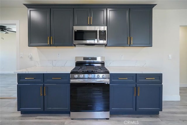 kitchen featuring stainless steel appliances, baseboards, light wood finished floors, light stone countertops, and a ceiling fan
