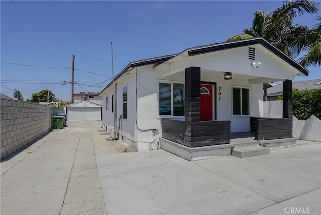 view of front of house with fence, a detached garage, an outdoor structure, stucco siding, and covered porch