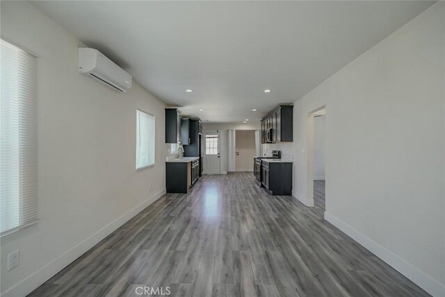 unfurnished living room featuring a wall unit AC, a sink, baseboards, wood finished floors, and recessed lighting