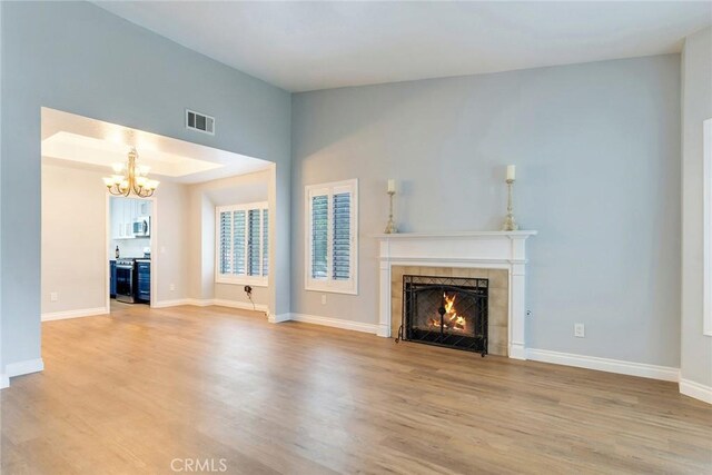 unfurnished living room featuring a tile fireplace, light wood-style floors, a chandelier, and baseboards