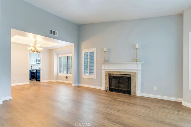 unfurnished living room with a chandelier, a tiled fireplace, light wood-style floors, and baseboards