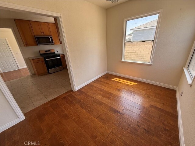 kitchen featuring stainless steel appliances, dark wood-style flooring, brown cabinets, and baseboards