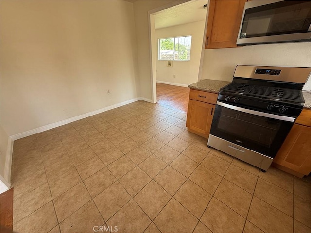 kitchen with stainless steel appliances, light tile patterned flooring, baseboards, light stone counters, and brown cabinets