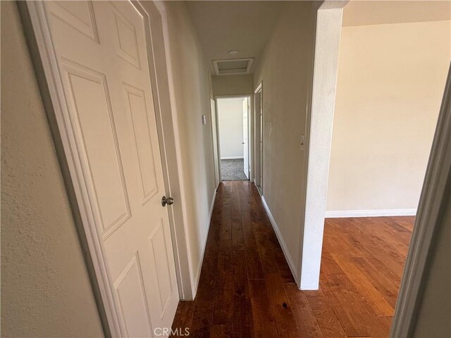 corridor featuring dark wood finished floors, baseboards, and attic access