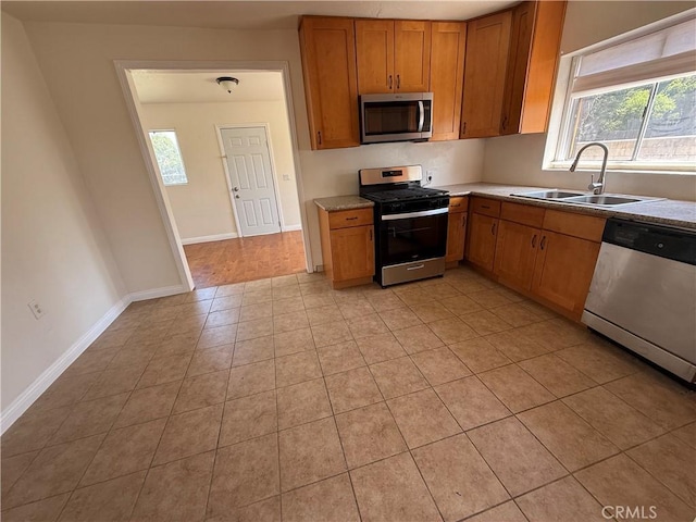 kitchen featuring appliances with stainless steel finishes, a sink, brown cabinetry, and light tile patterned flooring