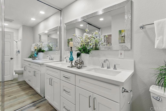 full bathroom featuring toilet, wood finished floors, a shower stall, double vanity, and a textured wall