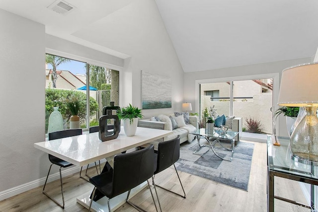 dining area featuring light wood-type flooring, baseboards, and high vaulted ceiling