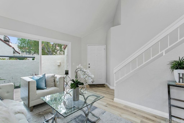 living room featuring light wood-style floors, stairs, baseboards, and lofted ceiling