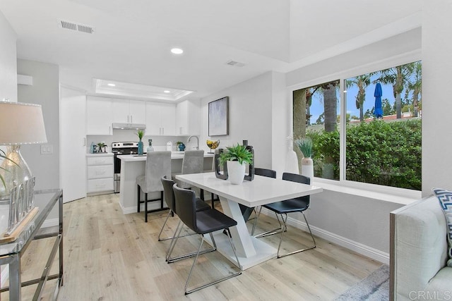 dining room with light wood-type flooring, baseboards, recessed lighting, and a raised ceiling