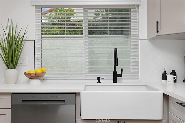 kitchen view of stainless steel dishwasher, a sink, backsplash, and light countertops