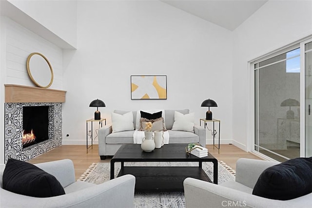 living area featuring high vaulted ceiling, a tile fireplace, wood finished floors, and baseboards