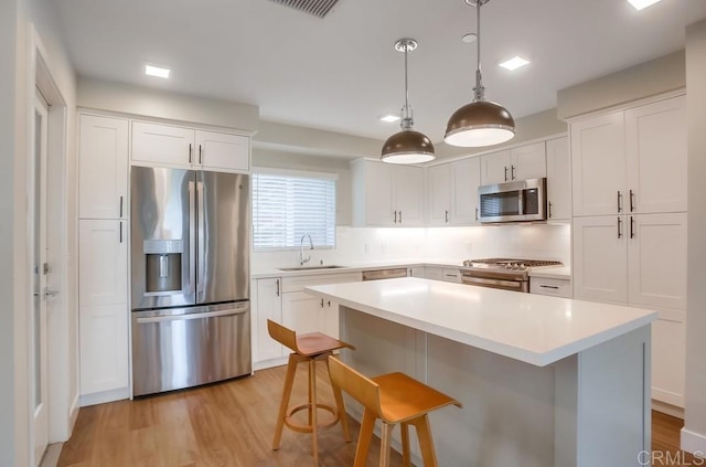 kitchen featuring appliances with stainless steel finishes, a sink, a center island, light wood-style floors, and white cabinets