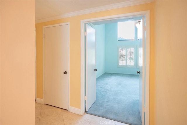 hall featuring crown molding, light tile patterned floors, baseboards, and light carpet