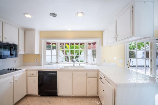 kitchen featuring black appliances, a sink, a peninsula, tile counters, and plenty of natural light