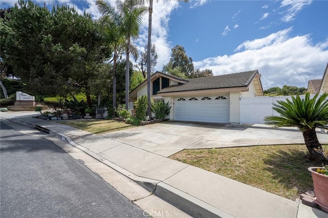 view of front facade featuring an attached garage, fence, a tiled roof, stucco siding, and driveway
