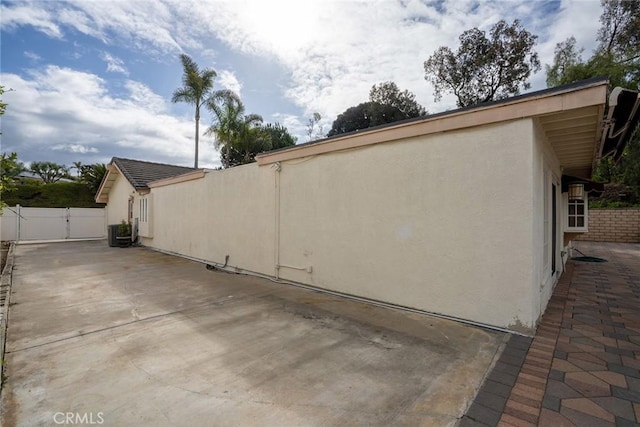 view of side of home with stucco siding, a patio, cooling unit, a gate, and fence