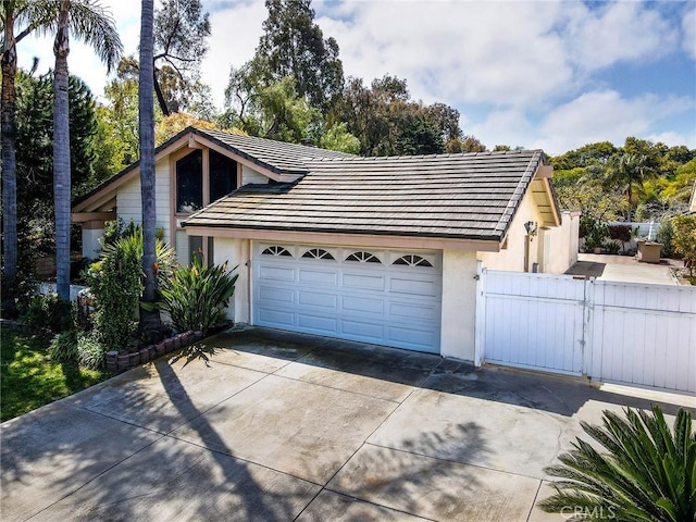 garage featuring concrete driveway, fence, and a gate