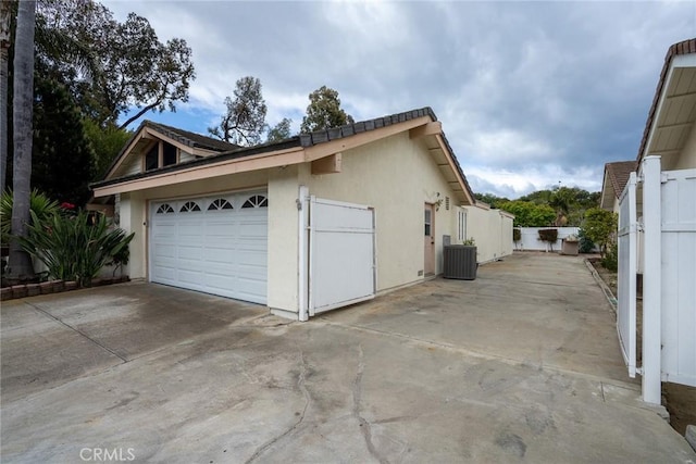 garage featuring driveway, fence, and cooling unit