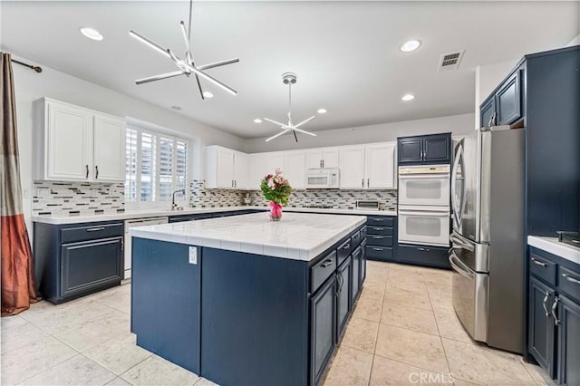kitchen with white appliances, a center island, white cabinets, light countertops, and decorative backsplash