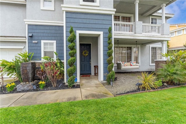 doorway to property with a balcony, stucco siding, and a lawn