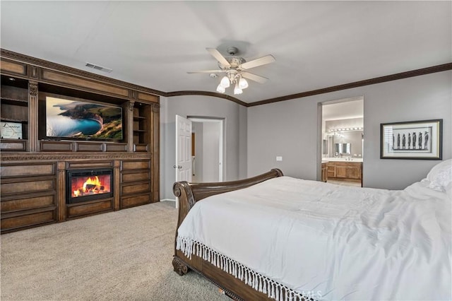 carpeted bedroom featuring crown molding, a glass covered fireplace, connected bathroom, and a ceiling fan