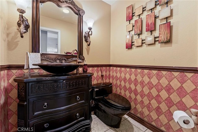 half bathroom with wainscoting, vanity, toilet, tile patterned flooring, and tile walls