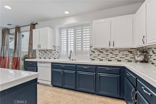 kitchen featuring white dishwasher, a sink, tile counters, white cabinets, and backsplash